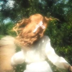 a blurry image of a woman with long hair sitting on the ground in front of trees