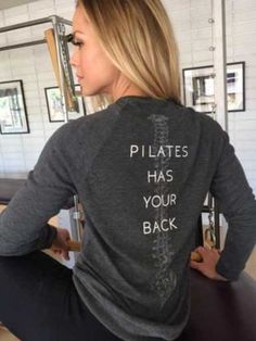 a woman sitting at a bar with her back turned to the camera, wearing a sweatshirt that says pilates has your back