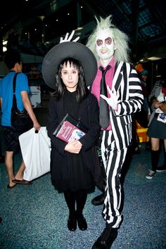 two people dressed up in costumes at an indoor event, one holding a book and the other wearing a costume