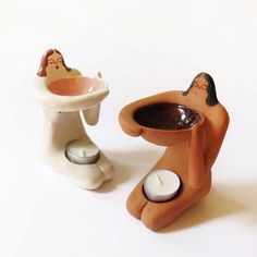 two ceramic figurines sitting next to each other on a white surface, one holding a candle