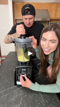 a man and woman are making something in a blender while they look at the camera