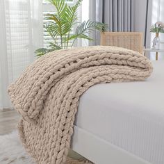 a bed with a blanket on top of it next to a chair and potted plant