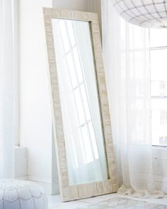 a large mirror sitting on top of a white floor next to a window in a room