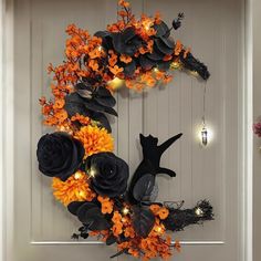 a halloween wreath with black cats and orange flowers on the front door, decorated with lights