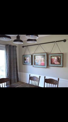 three framed pictures hang on the wall above a dining room table with four wooden chairs