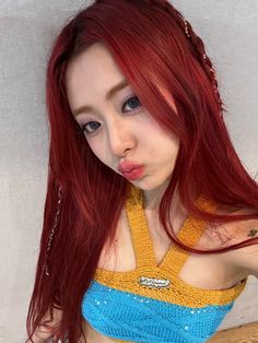 a woman with long red hair wearing a blue and yellow top posing for the camera