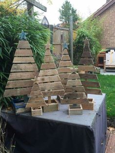 several wooden christmas trees sitting on top of a table in front of a yard with grass