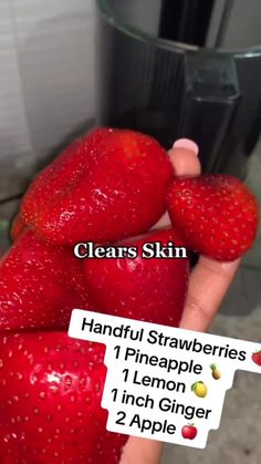 a person holding three strawberries in front of a blender with labels on them