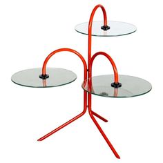 two glass tables with metal legs and an orange stand on one side, the other is round