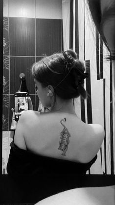 a woman with a tattoo on her back looking at herself in the bathroom mirror,