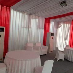 a room with tables, chairs and a white table cloth on the floor in front of a red curtained wall