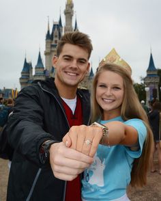 a man and woman posing for a photo in front of the castle at disney world