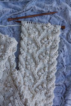 a white knitted scarf laying on top of a bed next to a knitting needle