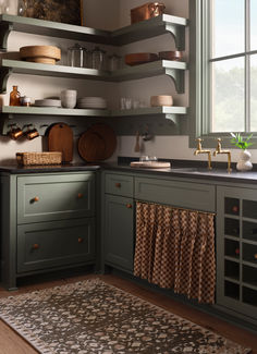 a kitchen with green cabinets and wooden flooring next to an open window on the wall