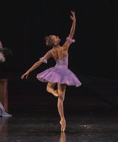 the ballerina is wearing a purple tutu and has her arms in the air