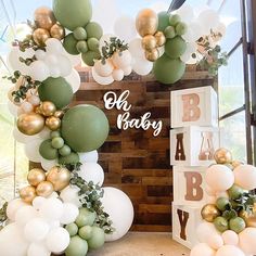 a baby shower with balloons and greenery on the wall next to it is decorated in gold, white and green colors