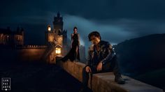 two people are sitting on a ledge in front of a castle at night with the lights on