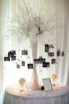 a table topped with a vase filled with white flowers and pictures hanging from the branches