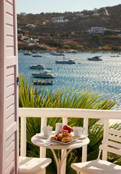 two white chairs sitting on top of a balcony next to a table with food and drinks