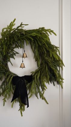 a wreath with bells hanging from it's side and evergreen leaves on the front