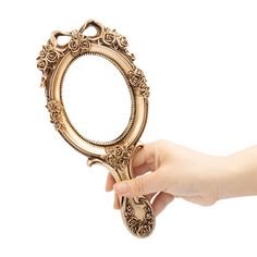 a hand holding a gold ornate mirror on a white background