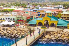 people are walking on the pier in front of some colorful buildings and blue ocean water