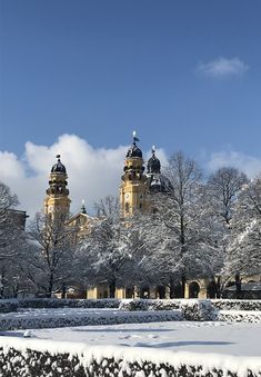 snow covers the ground and trees in front of a large building with two spires