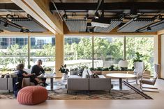 two people sitting on couches in an open room with large windows and potted plants