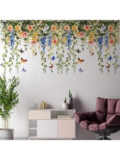 a living room with flowers and butterflies painted on the wall behind a purple chair in front of a white cabinet