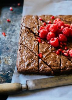 a chocolate cake with raspberries on top is sitting on a piece of parchment paper