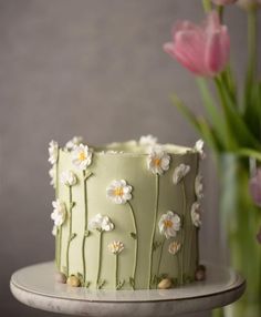 a green cake with white flowers on it and pink tulips in the background