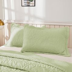 a bed with green sheets and pillows on top of it in a room next to a lamp