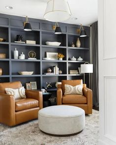 a living room with two leather chairs and a ottoman in front of a bookcase