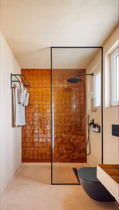 a bathroom with a glass shower door and brown tiles on the wall, along with a black bowl