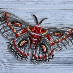 a beaded moth is sitting on a wooden surface and it's wings are spread out