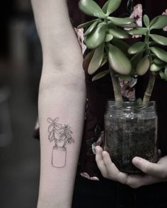 a person holding a plant in a jar on their left arm with a small tattoo on it