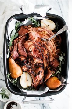 a roasting pan filled with meat, potatoes and pears on a marble table