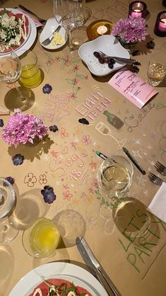 a table topped with plates of food next to wine glasses and flowers on top of it