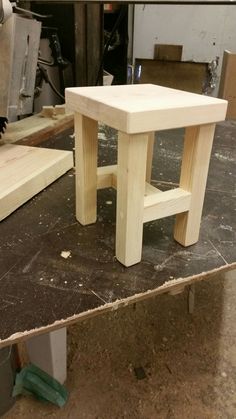 a wooden stool sitting on top of a piece of plywood in a shop area