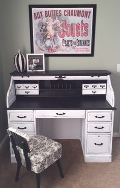 a white desk with black drawers and a chair in front of it, next to a framed poster on the wall