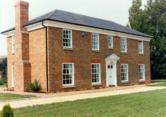 a large brick house with white windows on the front and side doors, in a grassy area