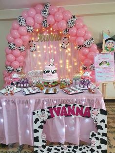 a table topped with lots of pink and white balloons next to a cow themed cake