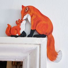 an orange fox and her cub are sitting on the mantle