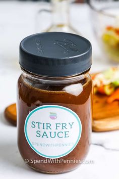 a jar filled with brown sauce sitting on top of a table next to a cutting board