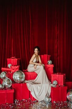 a woman sitting on top of red boxes surrounded by silver balls and confetti