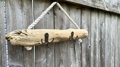 a piece of driftwood hanging from a rope on a wooden wall next to a fence