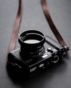 a camera with a lens attached to it's body on a black surface next to a brown leather strap