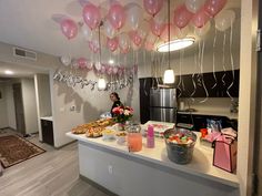 a woman standing in front of a table filled with food and balloons hanging from the ceiling