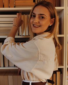 a woman standing in front of a bookshelf with her hand on the book shelf