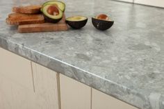 an avocado cut in half sitting on top of a counter next to bread